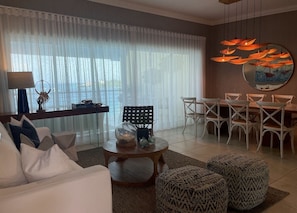 A modern living room with a sofa, coffee table, and ottomans. There is a dining area with chairs and a table. - Beautiful Apartment in Sosua with Maid included (Sosua)