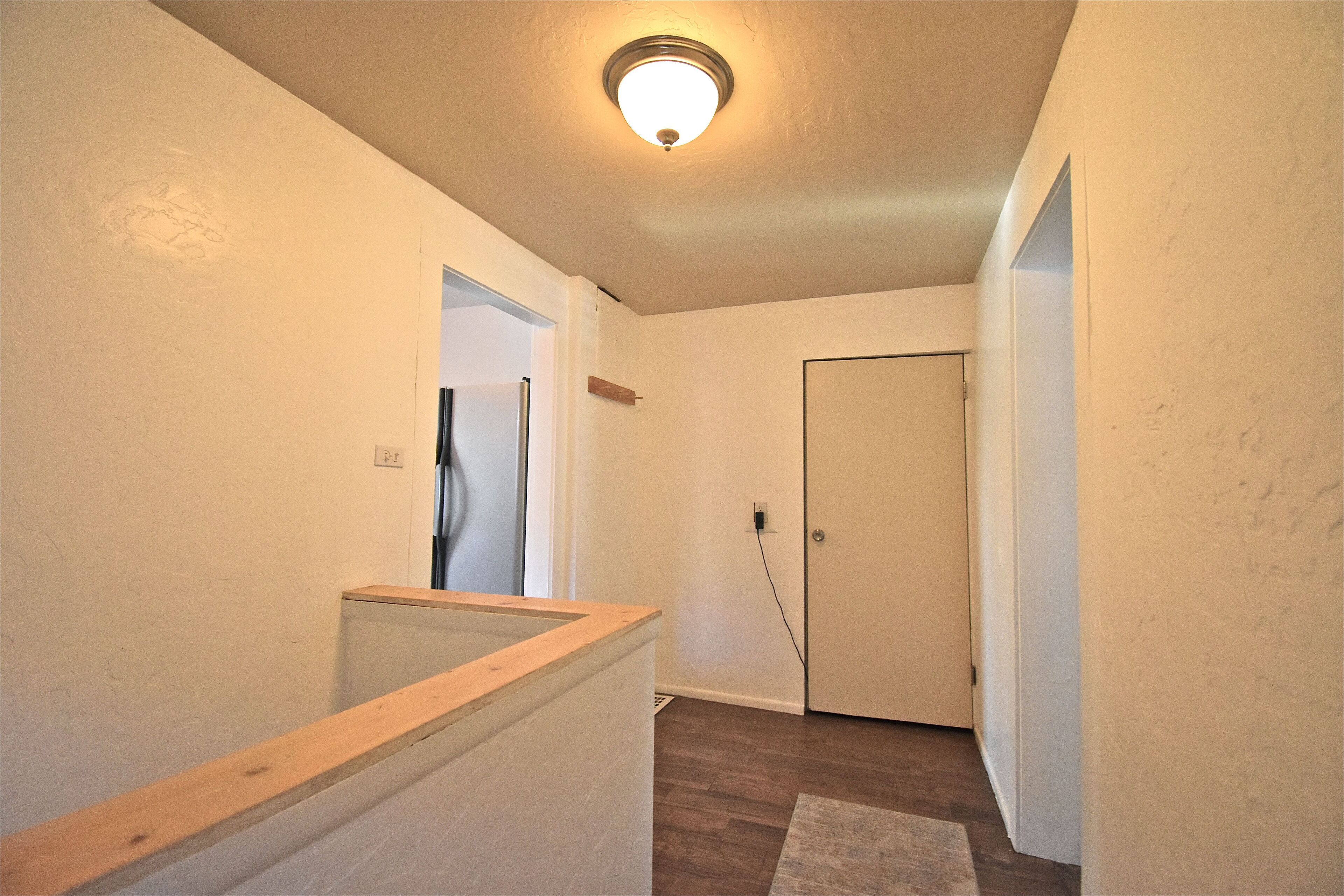 A narrow hallway with a wooden handrail, a door, and a light fixture on the ceiling.