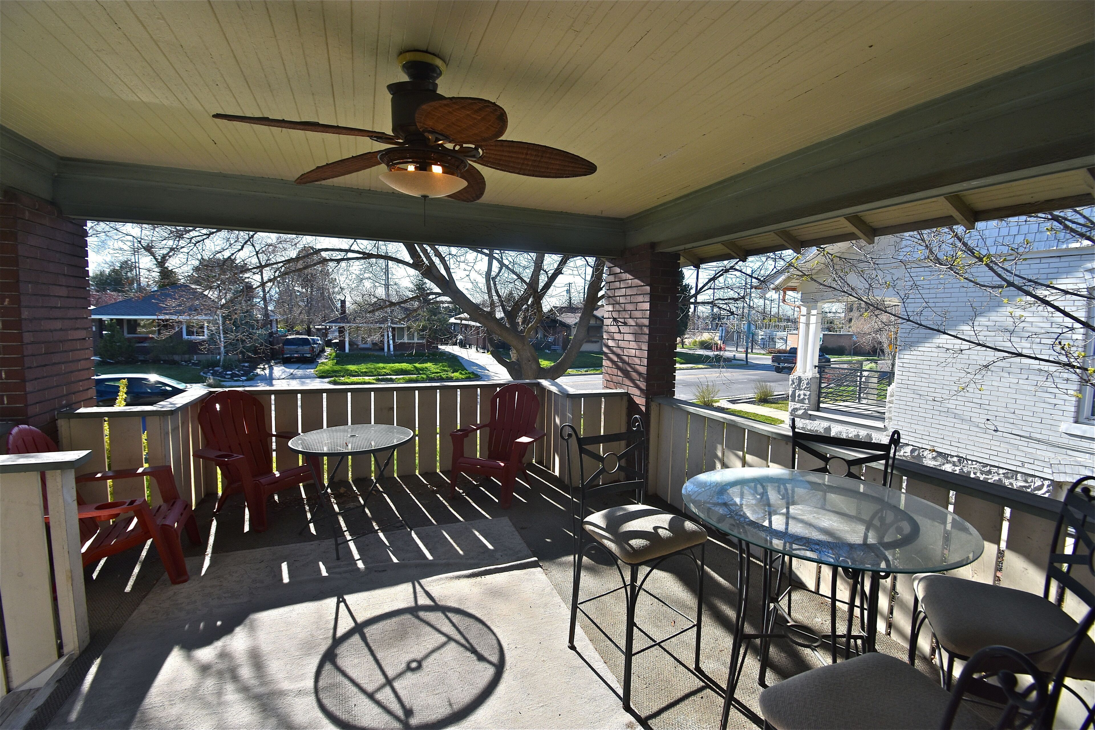 A covered outdoor patio with a ceiling fan, a glass table, and red chairs.