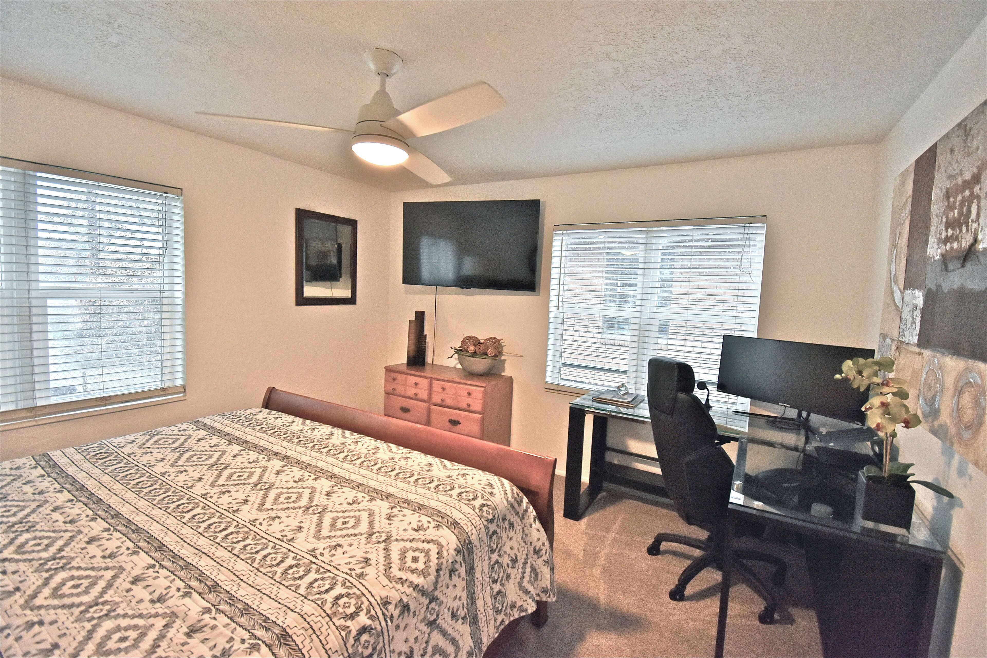 A bedroom with a bed, a desk, a chair, a TV, and a ceiling fan.