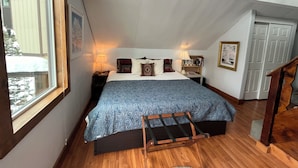 Quarto com cama, luminárias de cabeceira, uma escada de madeira, uma janela e uma porta.