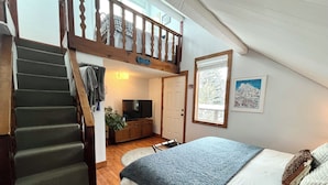 Quarto com cama, TV, escada e um mezanino com janela.