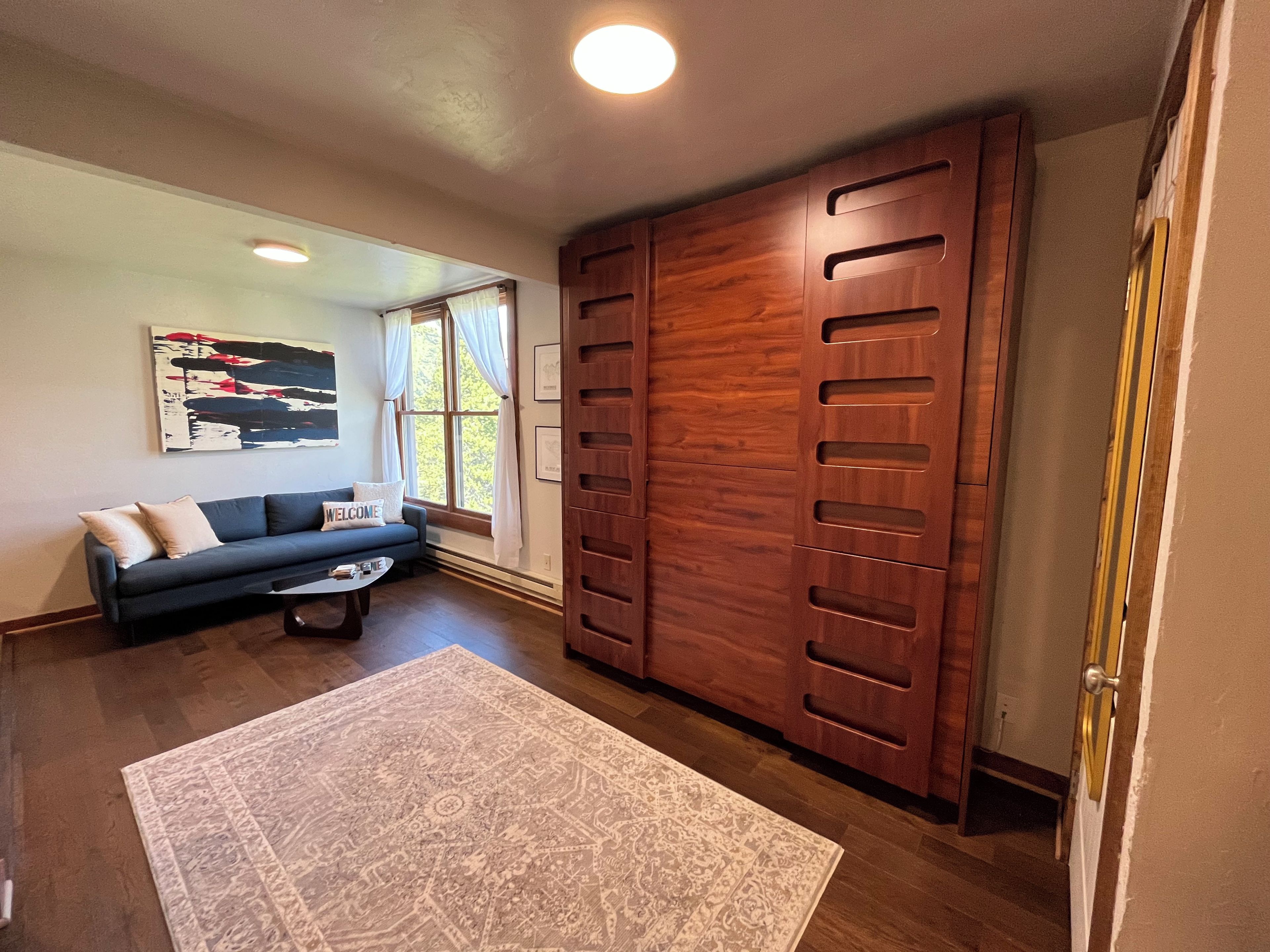 Un salon comprenant un canapé, une table basse, un tapis et une grande armoire en bois.