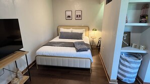 Une chambre à coucher comprenant un lit, un téléviseur, un ventilateur de plafond, une table de chevet et une étagère murale avec divers objets.