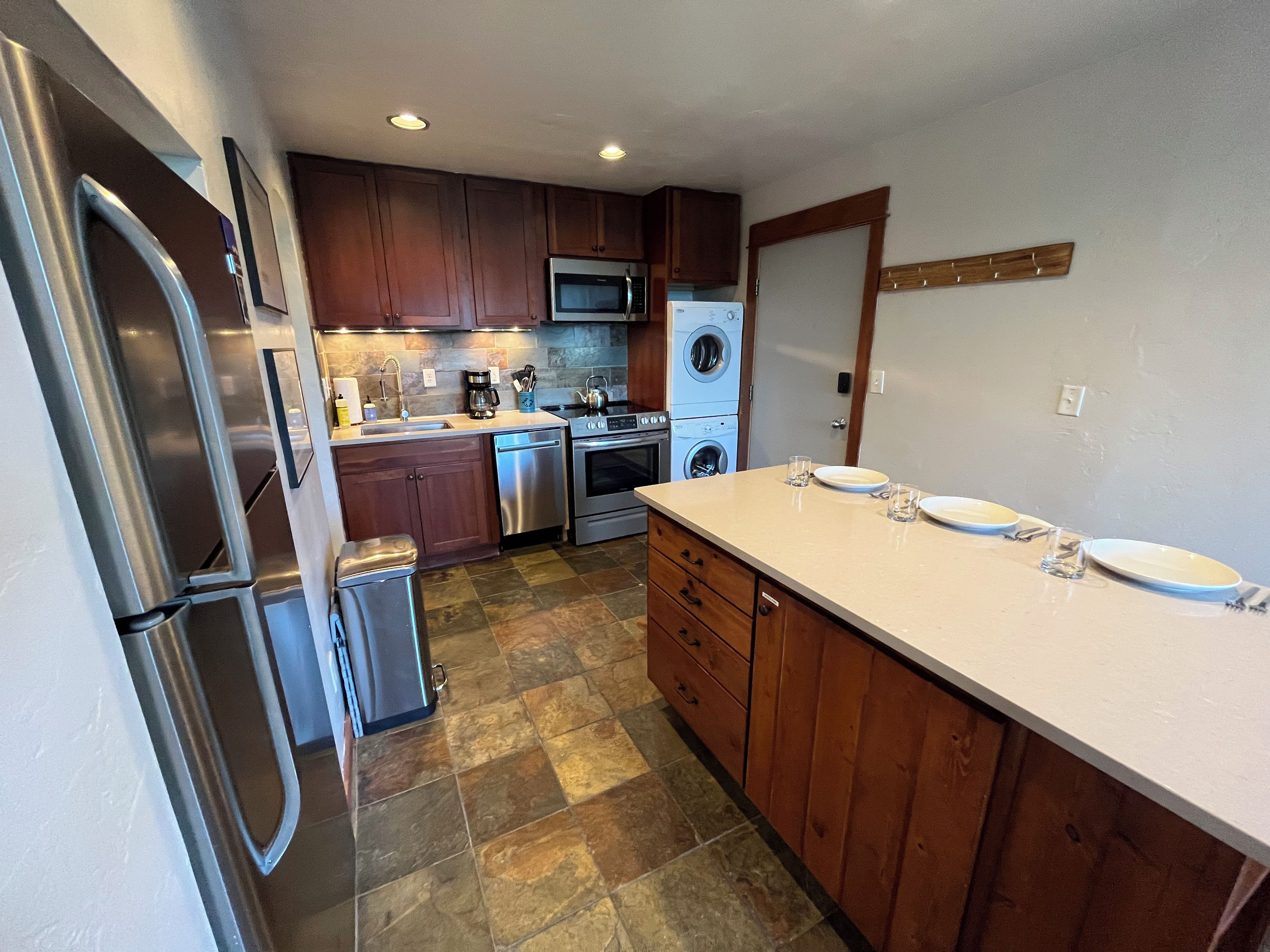 A kitchen with stainless steel appliances, wooden cabinets, and a stone tile floor.