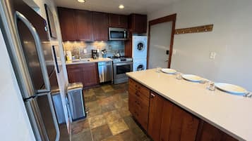 A kitchen with stainless steel appliances, wooden cabinets, and a stone tile floor.