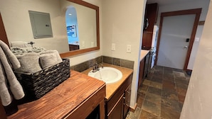 Une salle de bain avec un meuble-lavabo en bois, un grand miroir, un évier et un sol carrelé.