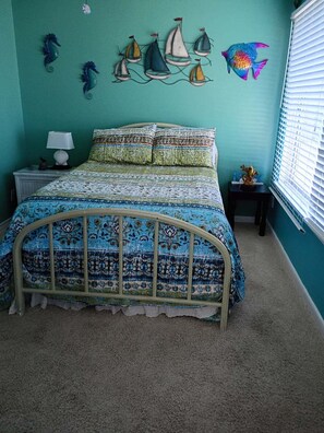 A bedroom with a bed, a nightstand, a lamp, a decorative wall art, and a window with blinds.