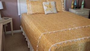 A neatly made bed with a patterned bedspread and pillows, a bedside table with a lamp, and a wall with framed pictures. - FALL RATES!  SURFS UP! Family friendly. Finance with Affirm! (Dauphin Island)