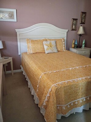 A neatly made bed with a patterned bedspread and pillows, a bedside table with a lamp, and a wall with framed pictures. - FALL RATES!  SURFS UP! Family friendly. Finance with Affirm! (Dauphin Island)