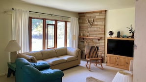 A living room with a beige sofa, a blue armchair, a wooden rocking chair, a fireplace, and a television. - Country Home, outdoor spaces, secluded but close to everything (Traverse City)