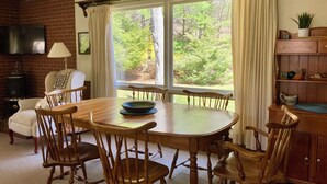 A dining area with a wooden table and chairs, a brick wall, a television, and a window with curtains. - Country Home, outdoor spaces, secluded but close to everything (Traverse City)