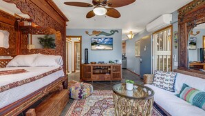 Una habitación amplia con una cama grande, un sofá, una mesa de centro y un televisor. Cuenta con un ventilador de techo, un espejo decorativo y un televisor de pared.
