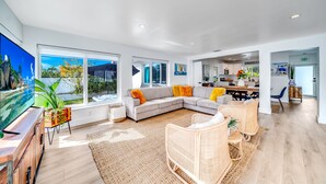 A spacious living area with a large sectional sofa, a flat-screen TV, and a dining area with wicker chairs and a wooden table. - Heated Pool+Hot Tub+Walk To Beach/Shops+Mini Golf! (Lauderdale-by-the-Sea)