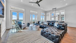 A spacious living room with a large sectional sofa, a fireplace, and a ceiling fan. - Foresight: Stunning Gulf Front Home, Private Pool w/ Spa, Guest House (Panama City Beach)