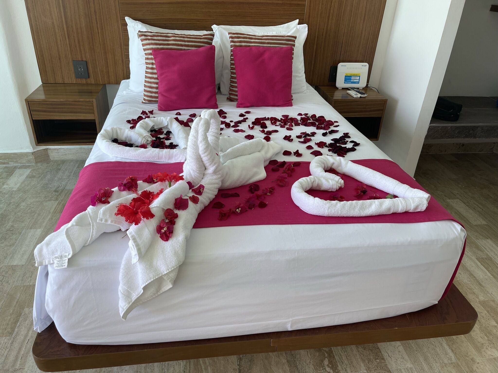Une chambre d’hôtel avec deux lits, chacun doté d’une tête de lit en bois, de draps blancs et d’oreillers roses.