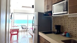 Eine Küche mit Holzausstattung, einem Kühlschrank, einer Mikrowelle und einer Kaffeemaschine. Ein Balkon bietet Meerblick.