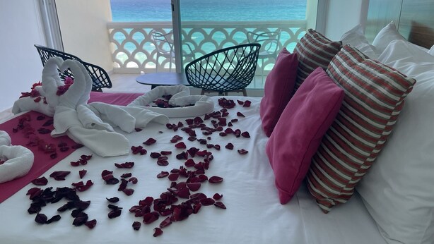Ein Hotelzimmer mit einem Bett, das mit Rosenblüten geschmückt ist, einer dekorativen Handtuchgestaltung und Blick aufs Meer.