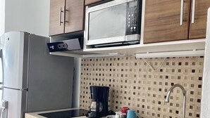 Eine moderne Küche mit Holzschränken, einem Edelstahlkühlschrank, einer Mikrowelle, einer Kaffeemaschine und einem Spülbecken.