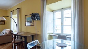 Ein Zimmer mit Glastisch, einer Couch, einer Lampe und einem Fenster mit Vorhängen.