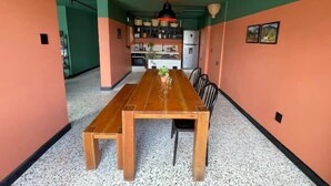 A dining area with a wooden table and chairs, a red pendant light, and a kitchen in the background. - La Bonita Guesthouse  (Bucaramanga)