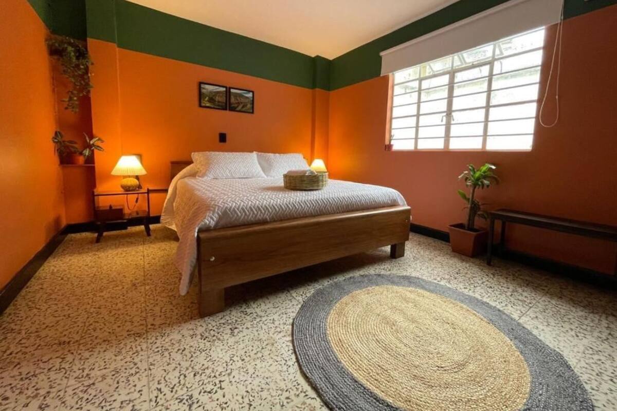A bedroom with a bed, two bedside tables, a window with blinds, and a floor rug.