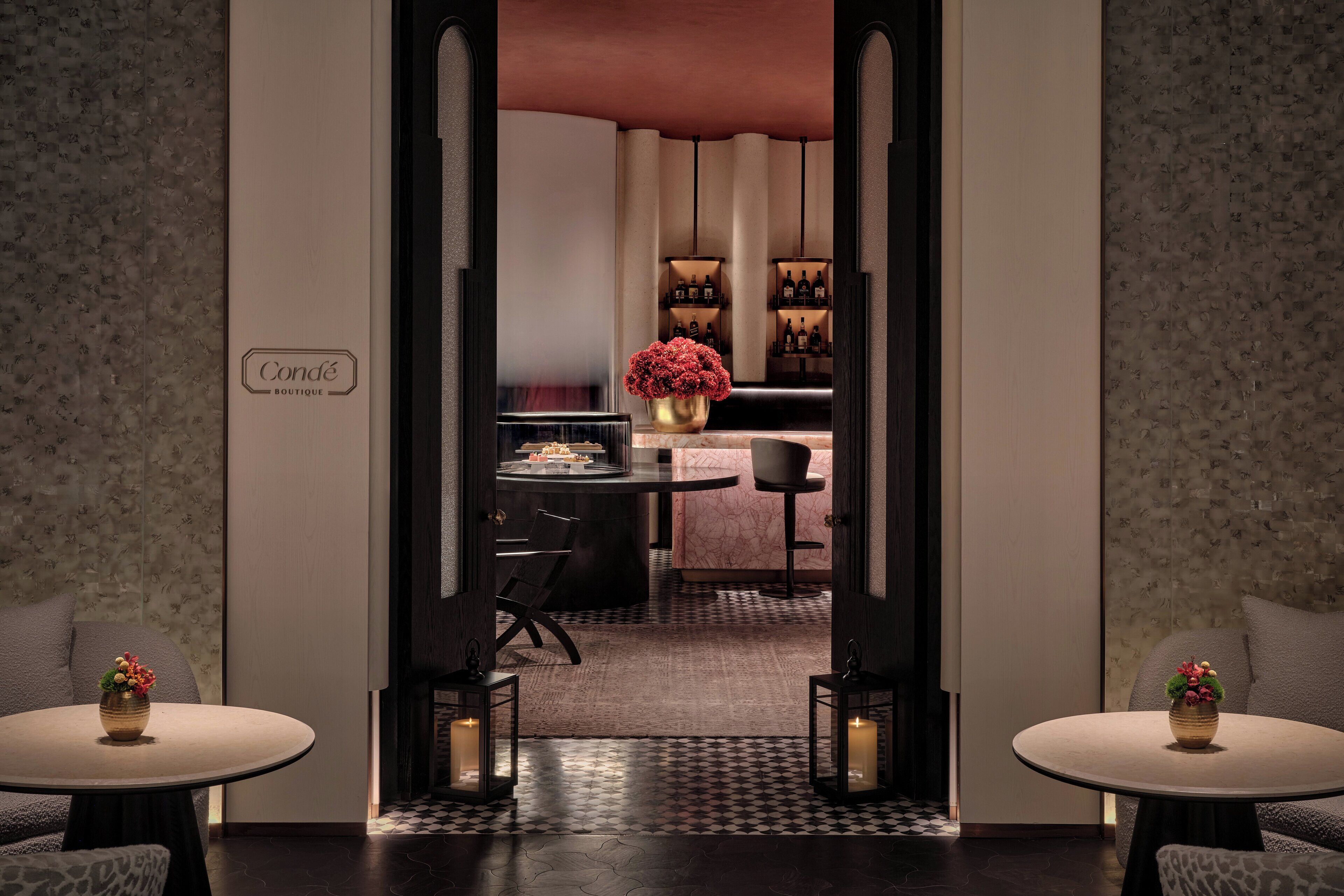 A hotel lobby with a central bar area, a seating area with two round tables, and a sign reading "Condé Boutique".