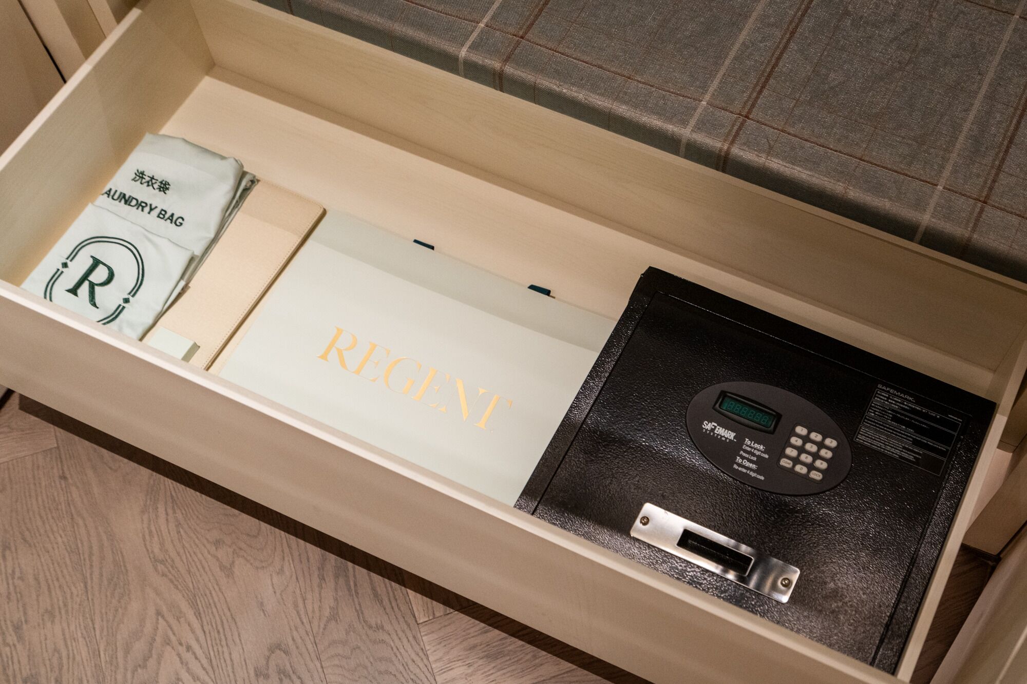 A drawer containing a white bag labeled "AUNDRY BAG," a white box with "REGENT" printed on it, and a black safe with a keypad.