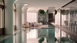 A modern indoor pool area with a clear pool, seating by the pool, and a marble wall with a green spherical decoration. - Regent Shanghai On The Bund (Shanghai)