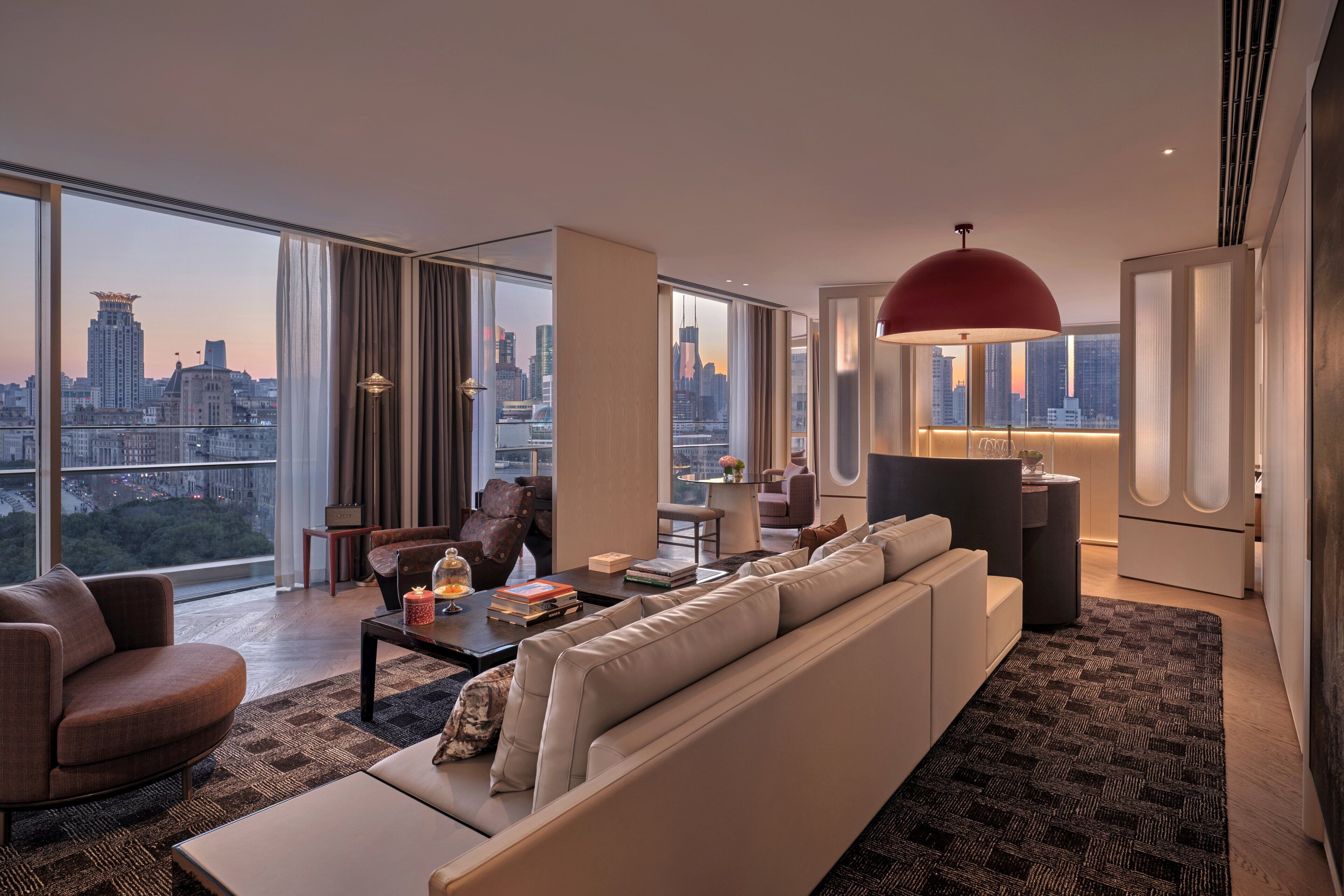 Una sala de estar moderna con un sofá grande, una mesa de centro y vistas a un paisaje urbano a través de ventanales de gran altura.