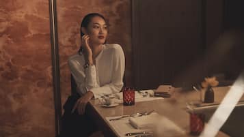 Une personne assise à une table, devant un carnet, une tasse et des couverts.
