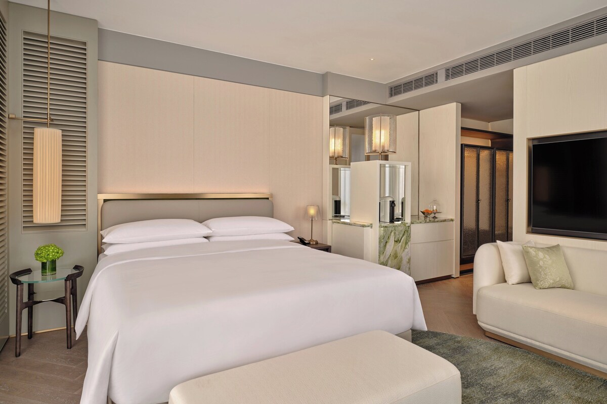 A modern hotel room with a large bed, a sofa, a TV, and a small table with a vase.