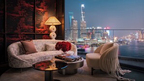 A modern living room with a sofa, armchair, and coffee table, featuring a cityscape view through large windows. - Regent Shanghai On The Bund (Shanghai)