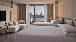 A hotel room with two beds, a sofa, a TV, and a view of a city skyline. - Regent Shanghai On The Bund (Shanghai)