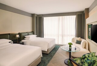 A hotel room with two beds, a sofa, a glass coffee table, and a TV.