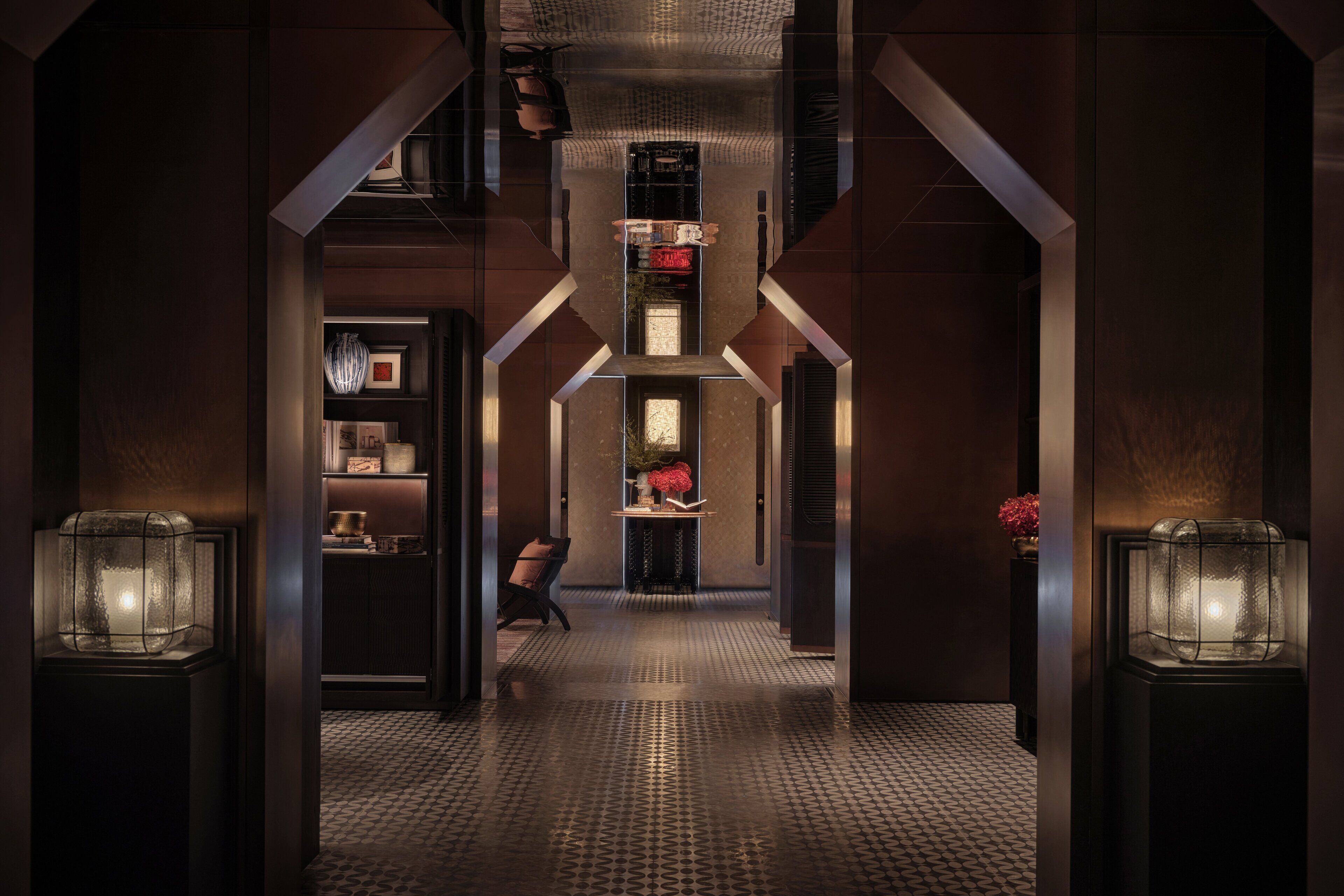 A hallway with a patterned floor, a chair, and a table with a vase.