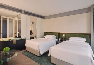 A hotel room with two beds, a glass table with a plant, a marble-topped desk, and a large mirror.