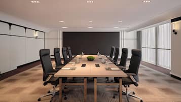 Un salón de conferencias con una larga mesa, sillas negras y una planta verde como centro de mesa.