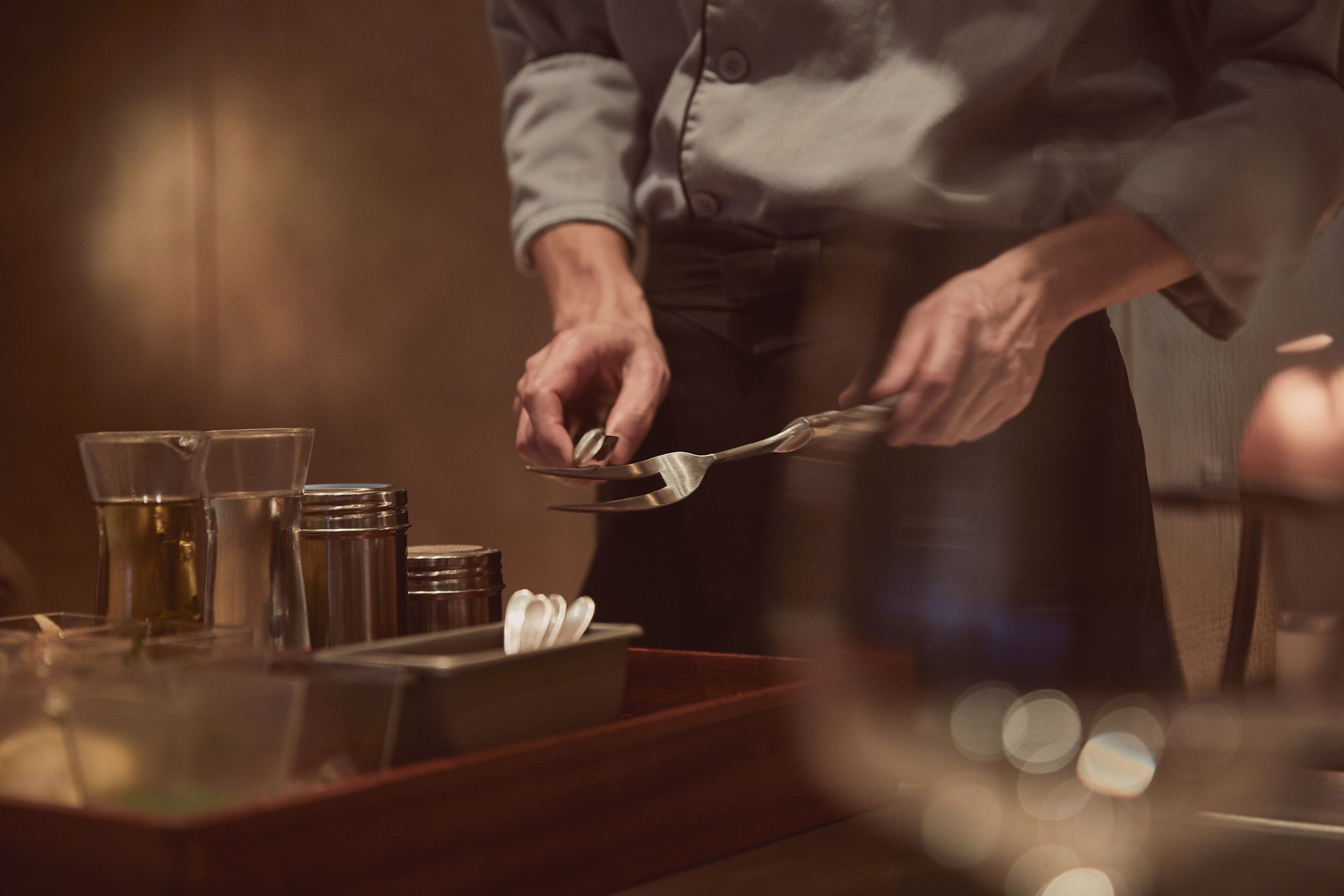 A person cutting a piece of paper with scissors on a table with a glass and a container.