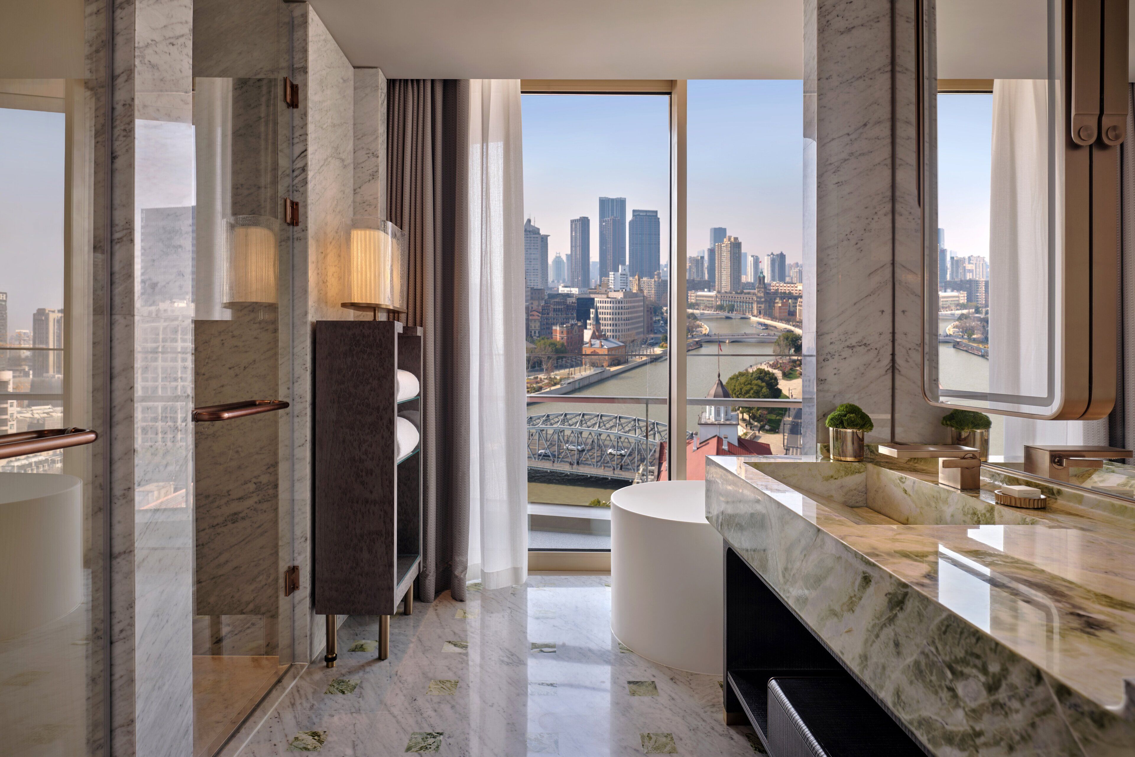 A modern bathroom with a large window, marble countertops, and a city view.