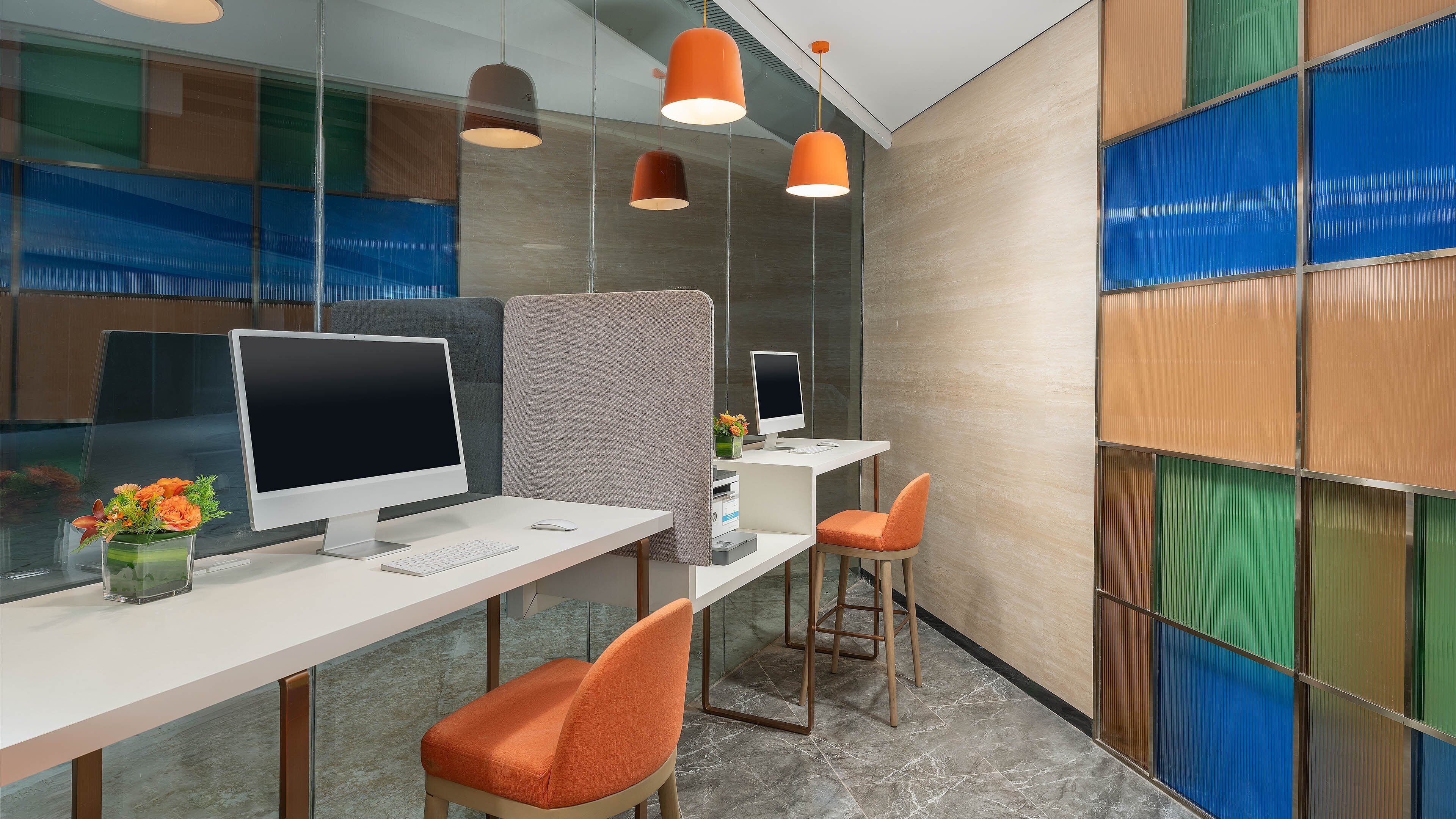 Un espacio de oficina moderno con un escritorio blanco, dos sillas naranjas, una computadora y un jarrón decorativo con flores.