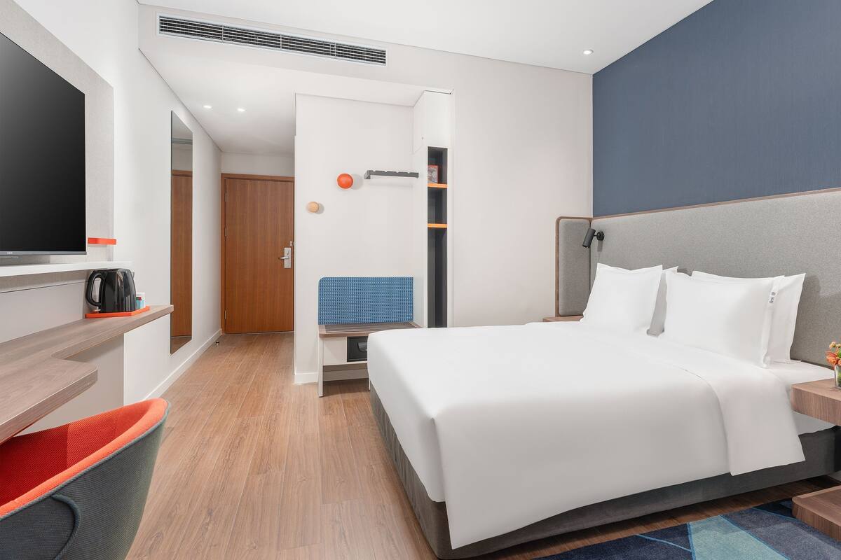 A modern hotel room with a large bed, a TV, a coffee maker, and a desk with a chair.