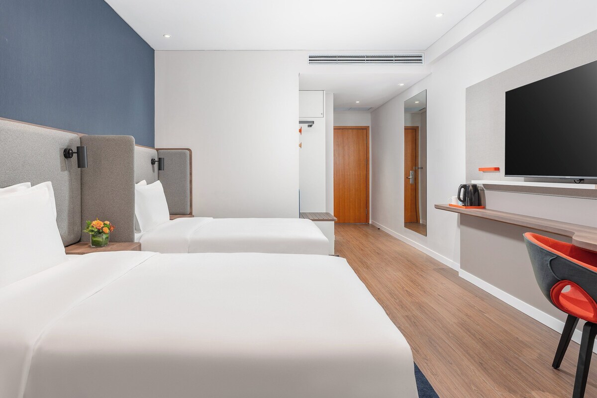 A hotel room with two beds, a TV, a coffee machine, and a small table with flowers.