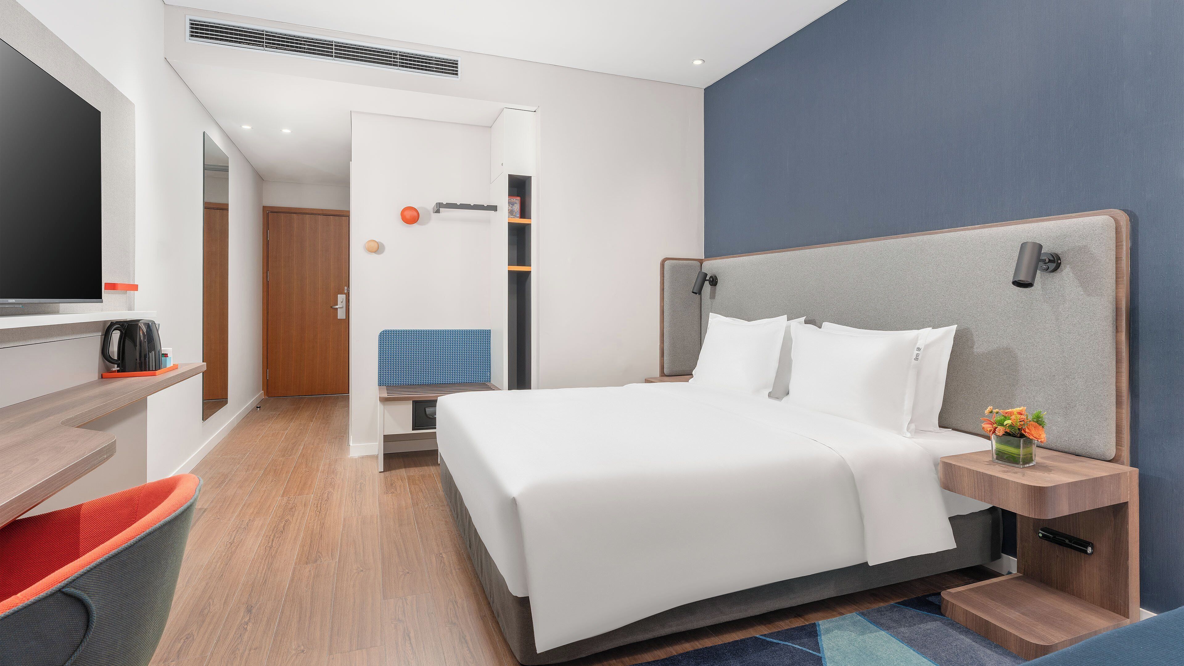 A modern hotel room with a large bed, a TV, a coffee maker, and a desk with a chair.