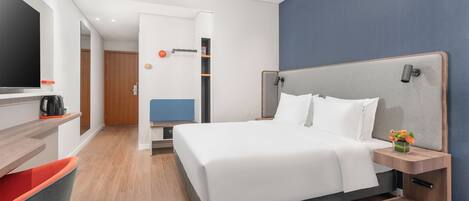 A modern hotel room with a large bed, a TV, a coffee maker, and a desk with a chair.