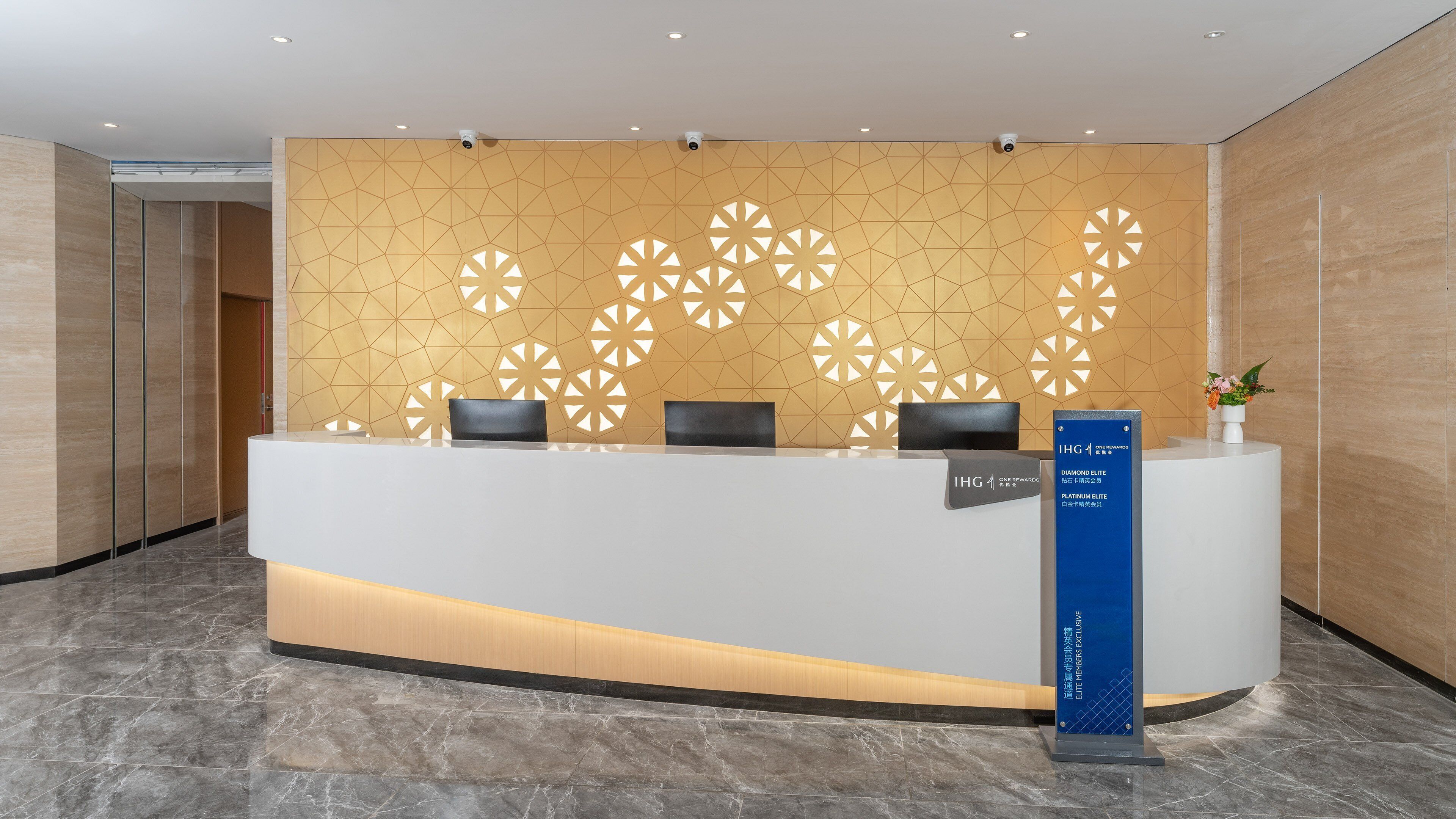 Een receptiebalie met een wand met een geometrisch patroon, een blauw bord waarop 'Diamond Elite' en 'Platinum Elite' vermeld staan, en een plantje aan de rechterkant.
