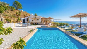 Une piscine avec des chaises longues, un espace patio et une vue sur l’océan.