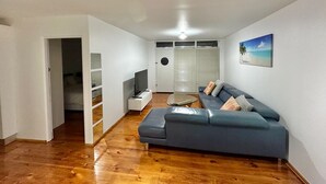 Una sala moderna con un sofá azul, piso de madera y un cuadro de una playa.