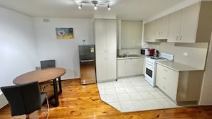 Cocina compacta con gabinetes blancos, estufa a gas, microondas y refrigerador. Hay una mesa de comedor con sillas y piso de madera.