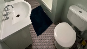 Un baño con lavamanos blanco, inodoro y ducha con mampara de vidrio.